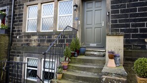 A brick building with a grey door, a staircase, and potted plants on the steps. - Relax in the Heart of Bronte Country (Haworth)