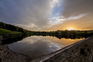 A calm lake reflecting the sky and surrounding landscape, with a stone bridge and a gazebo in the distance.