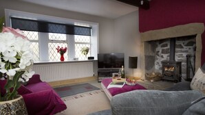 A living room with a stone fireplace, a television, and a window with flowers. - Relax in the Heart of Bronte Country (Haworth)