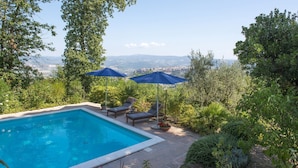 A swimming pool with two lounge chairs and two umbrellas, surrounded by lush greenery and a view of distant mountains. - Villa Ombrosa 8, Emma Villas (Porano)