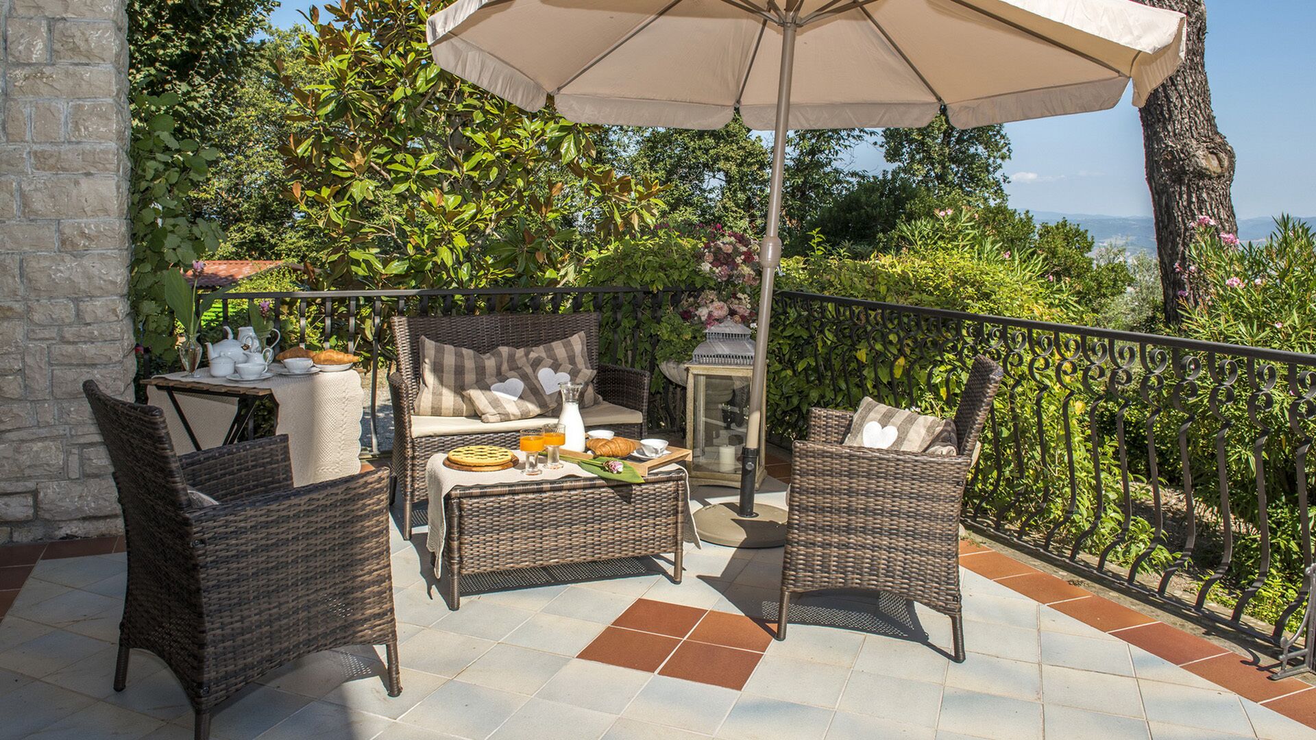 Une terrasse avec des meubles en osier, une table dressée pour le petit-déjeuner et une vue sur la mer.