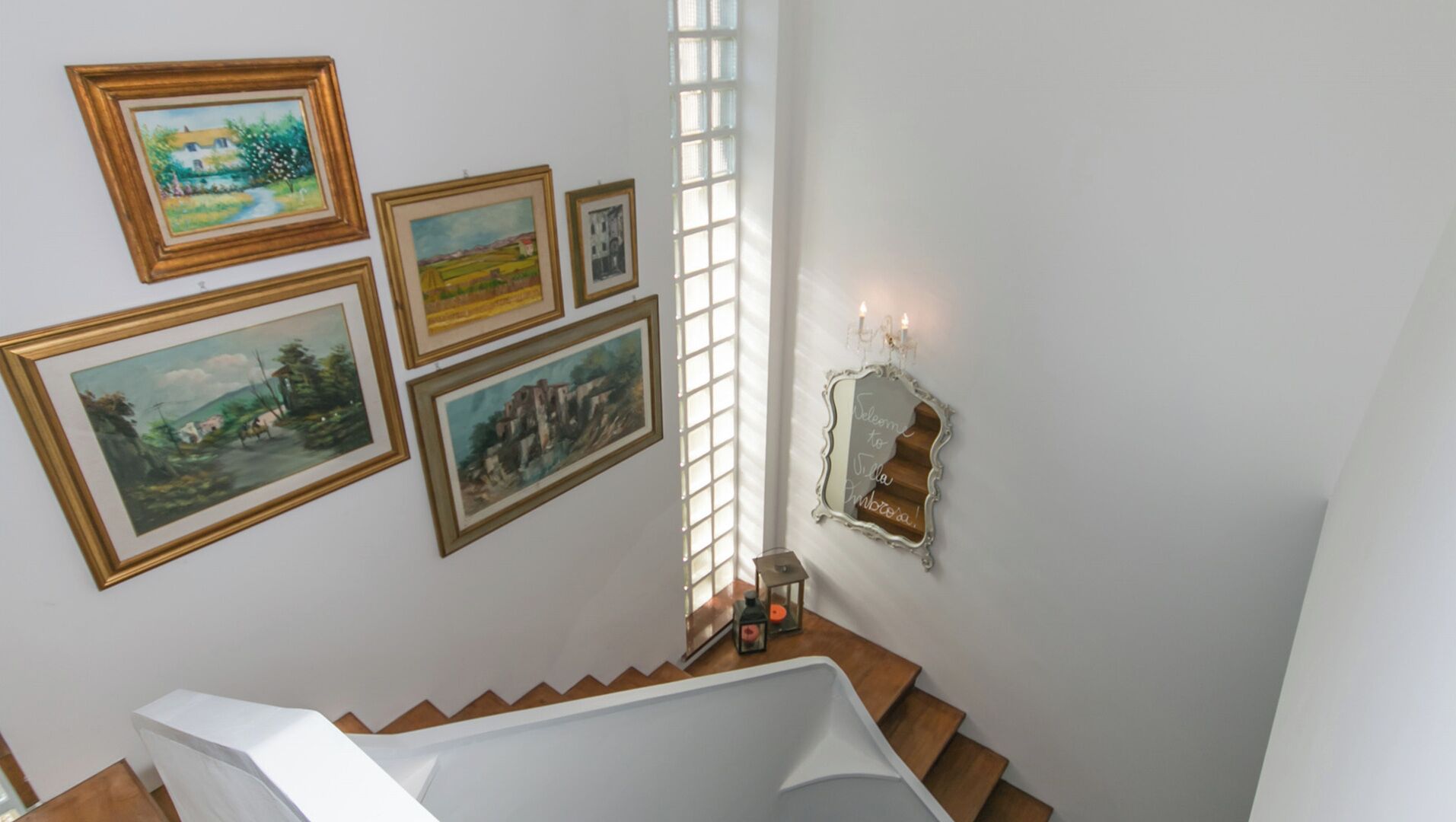 Una escalera con vista al piso superior, donde varias pinturas enmarcadas adornan la pared.