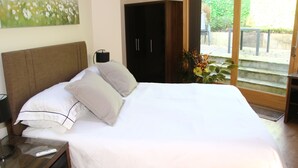 Habitació d'hotel amb un llit gran, una tauleta de nit, un comandament a distància, un armari fosc i una porta corredissa de vidre que dona a una zona exterior.