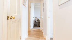 A hallway with white walls, wooden flooring, and framed artwork.