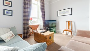 A living room with a sofa, a wooden chest, a television, and a chair.