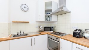 A modern kitchen with white cabinets, stainless steel appliances, a wooden countertop, and a clock on the wall.