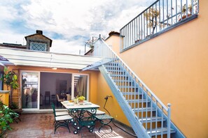 Un patio con una mesa, sillas, una escalera y un edificio con pared amarilla.