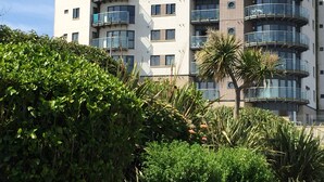 Un immeuble résidentiel à plusieurs étages, doté de balcons, surmonté d’une structure en forme de dôme et entouré de verdure.