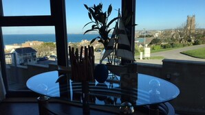 Un coin repas avec une table en verre, une plante et une vue sur la mer et les bâtiments.