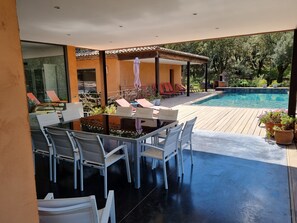 A modern outdoor dining area with a glass table and white chairs, overlooking a swimming pool and lush greenery. - House / Villa - Plan de la Tour (Le Plan-De-La-Tour)
