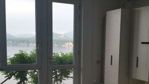 Un vaste salon doté d’une grande porte-fenêtre coulissante donnant sur un balcon qui offre une vue sur un plan d’eau et sur des collines lointaines.