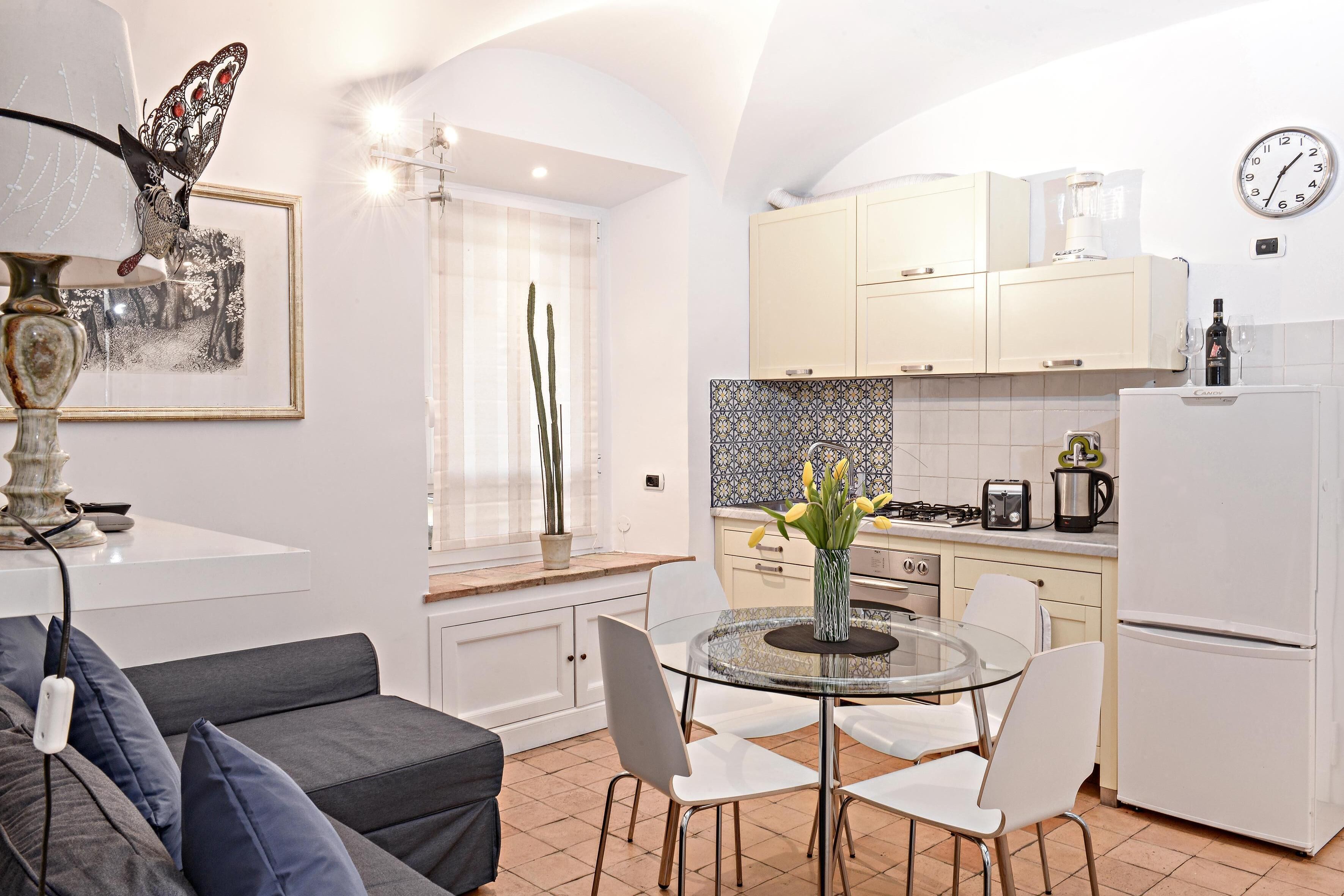 Una cocina moderna con armarios blancos, una mesa de comedor con superficie de vidrio y un refrigerador.