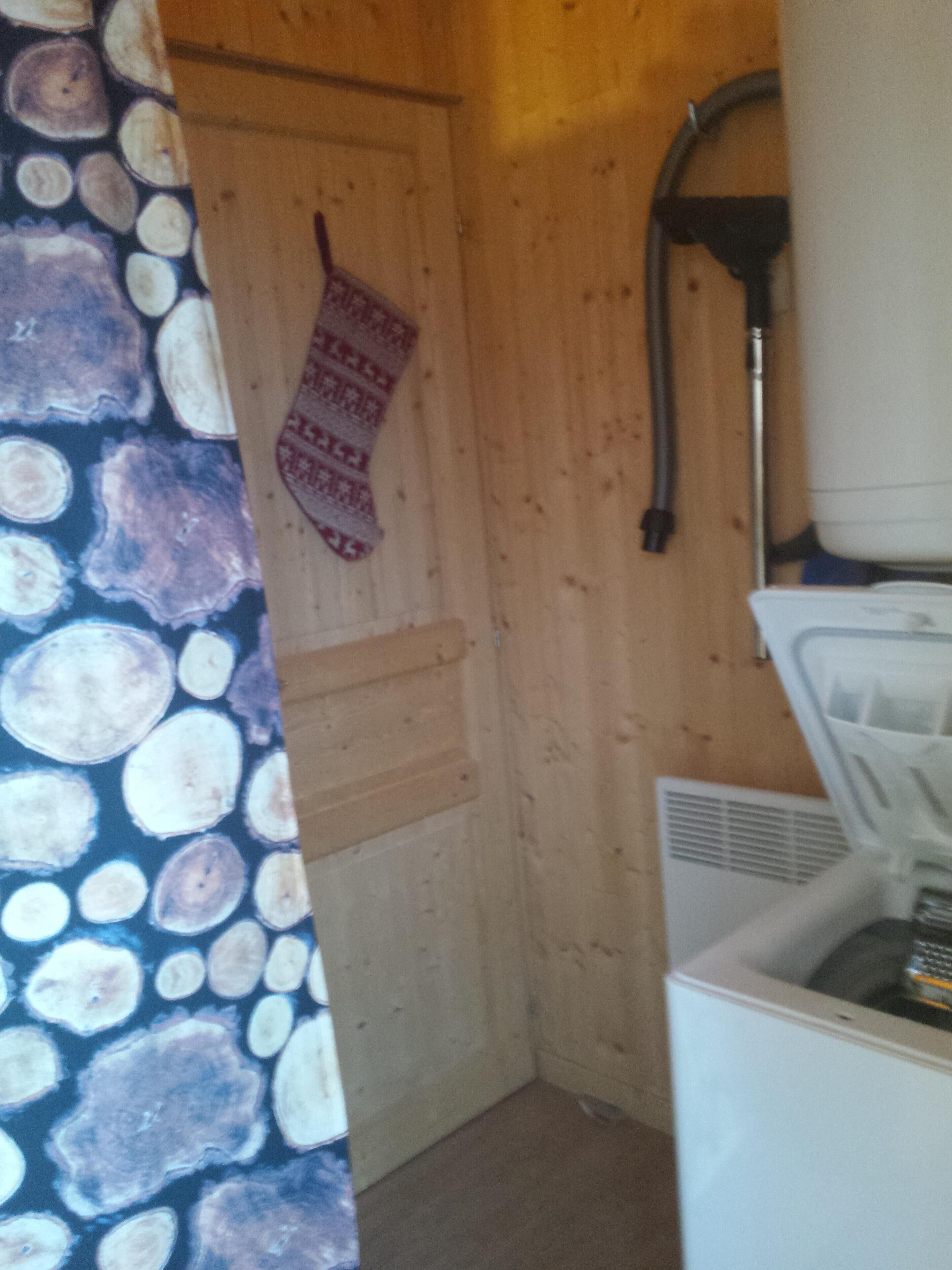Une petite pièce, de taille modeste, avec une porte en bois, un rideau à motifs, un radiateur et un appareil électroménager blanc, probablement un lave-linge.