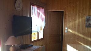 Una habitación de madera con un televisor sobre un mueble de madera, una puerta y una pequeña mesa con diseño de corazón.