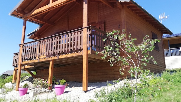 Una cabaña de madera con balcón, rodeada de follaje y rocas.