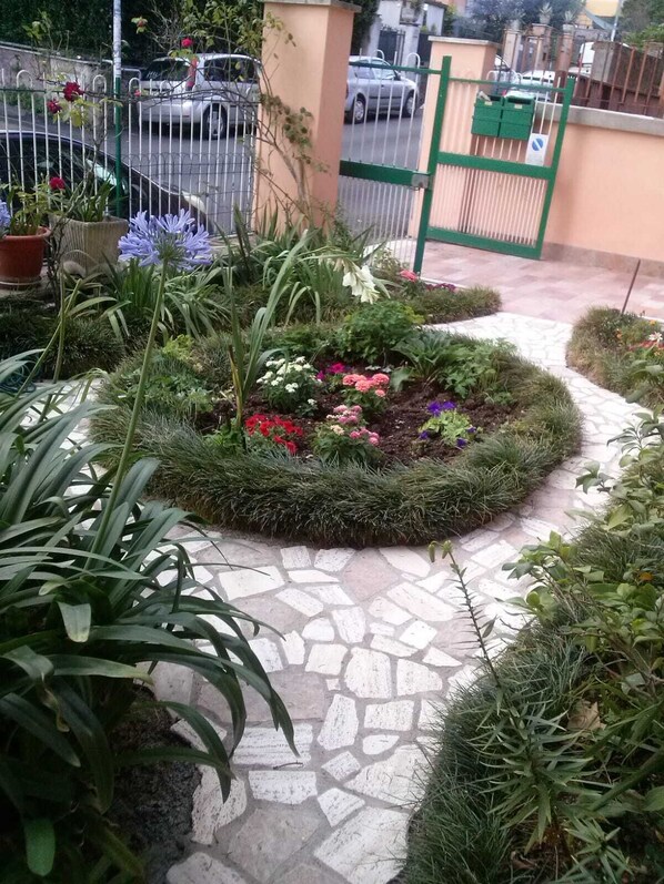 A garden area with a variety of plants and flowers, a paved walkway, and a metal gate.
