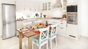 A modern kitchen with white cabinetry, a stainless steel refrigerator, a gas stove, and a built-in oven.