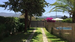 Un sendero en el jardín que conduce a una zona de piscina con cerca de madera y abundante vegetación.
