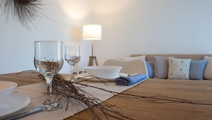 Una mesa de comedor con dos copas de vino, un bol y una lámpara en una sala de estar con un sofá y cojines.