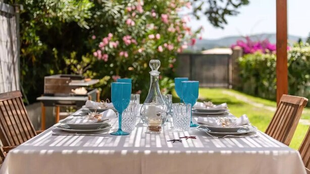 Mesa de comedor exterior con vajilla azul y platos, rodeada de sillas de madera.
