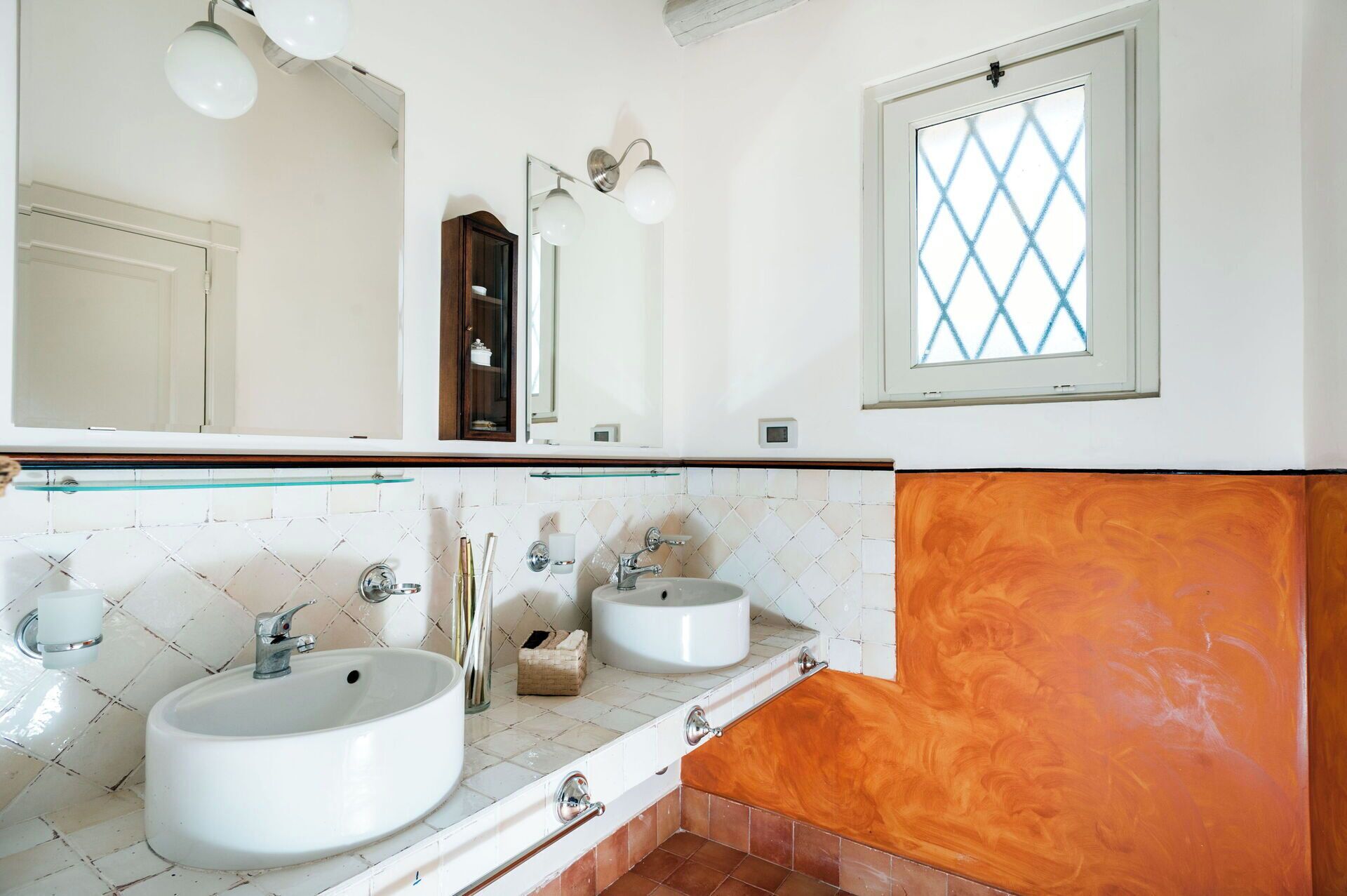 A bathroom with two sinks, a large mirror, and a window with a diamond pattern.
