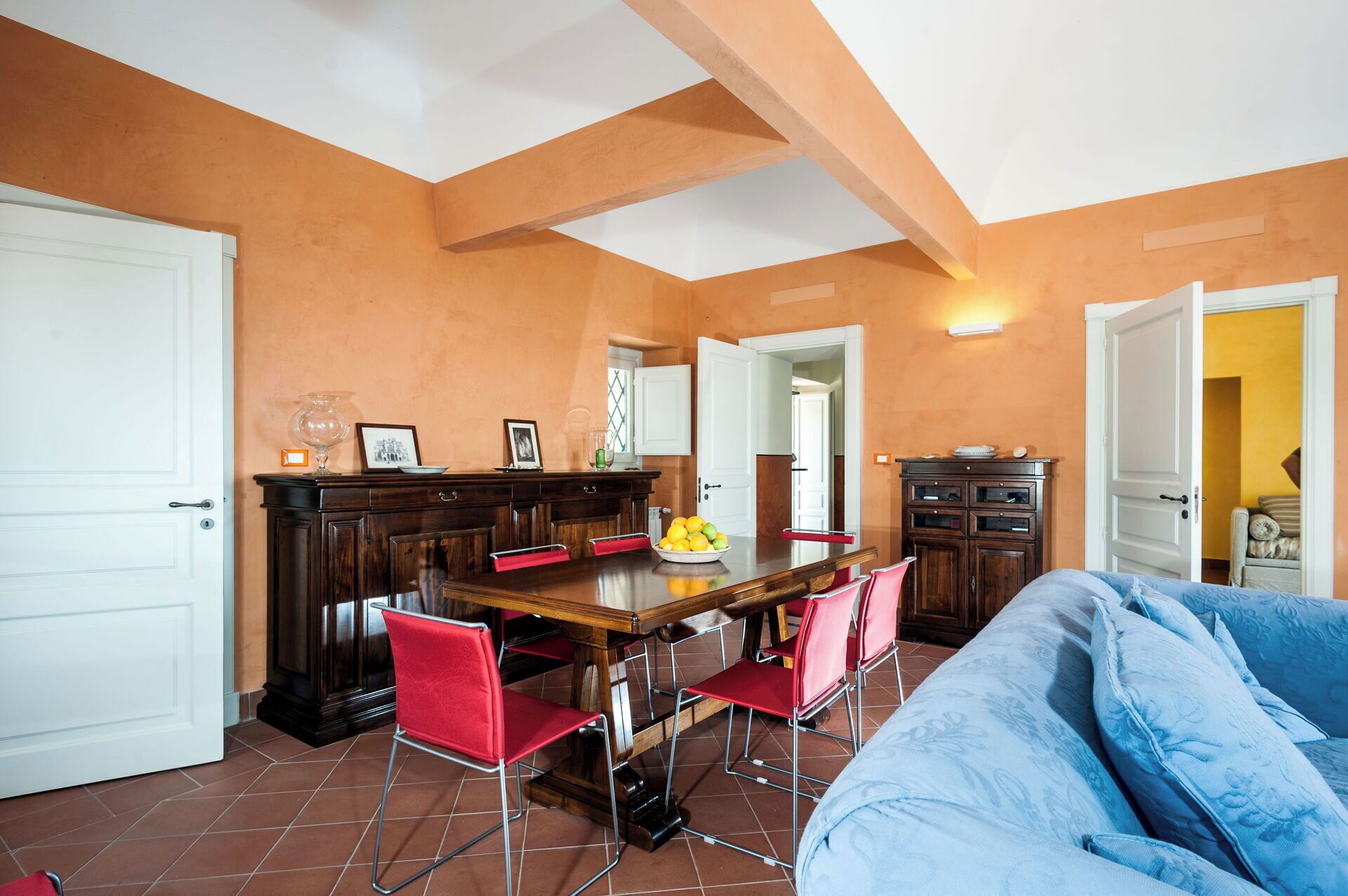Un coin repas avec une table en bois, des chaises rouges et une cuisine en arrière-plan.