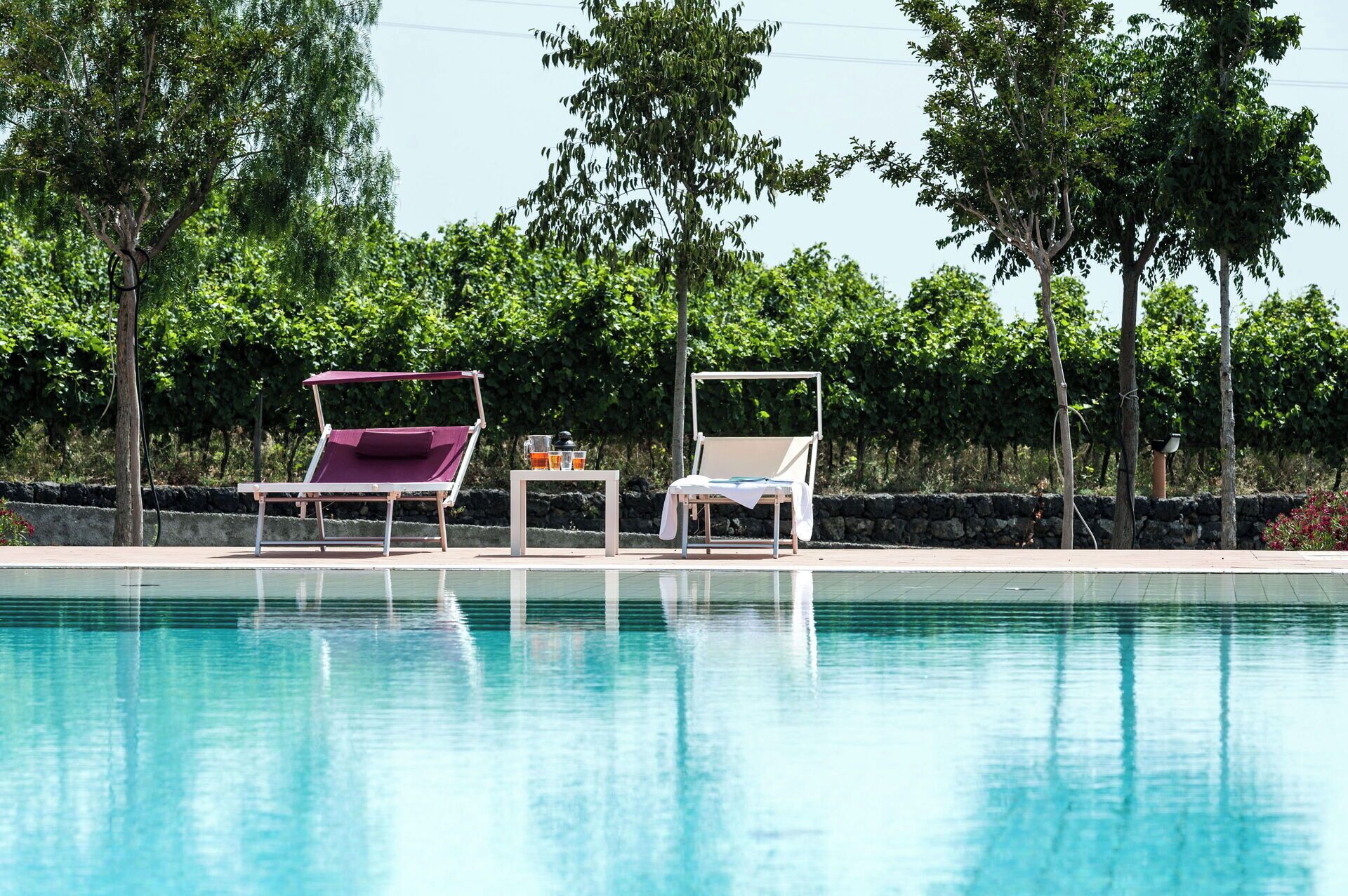 A swimming pool with two sun loungers and a table with drinks.
