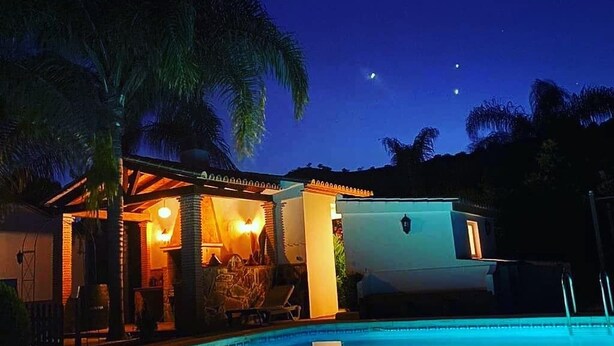 A nighttime pool area with a lounge chair and a small building with lights.