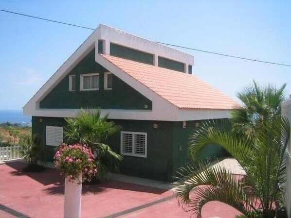 Uma casa de dois andares com telhado inclinado, varanda e vista para o mar.