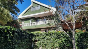 Uma casa de dois andares com fachada verde, grades de varanda brancas e uma pequena janela no andar superior.