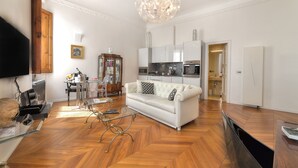 Una sala de estar moderna con un sofá blanco, suelo de madera, una mesa de centro de vidrio y un televisor de pantalla plana grande.