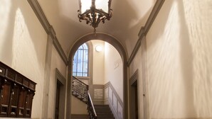 Un amplio pasillo con candelabro, escalera y suelo estampado.