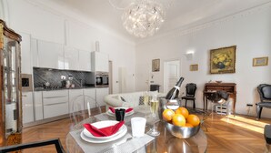 Una cocina moderna con armarios blancos, un comedor con mesa de vidrio y una sala de estar con sofá y un cuadro.