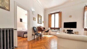 Amplia sala de estar con piso de madera tipo espiga, un sofá blanco, una mesa de comedor con sillas y un televisor montado en la pared.