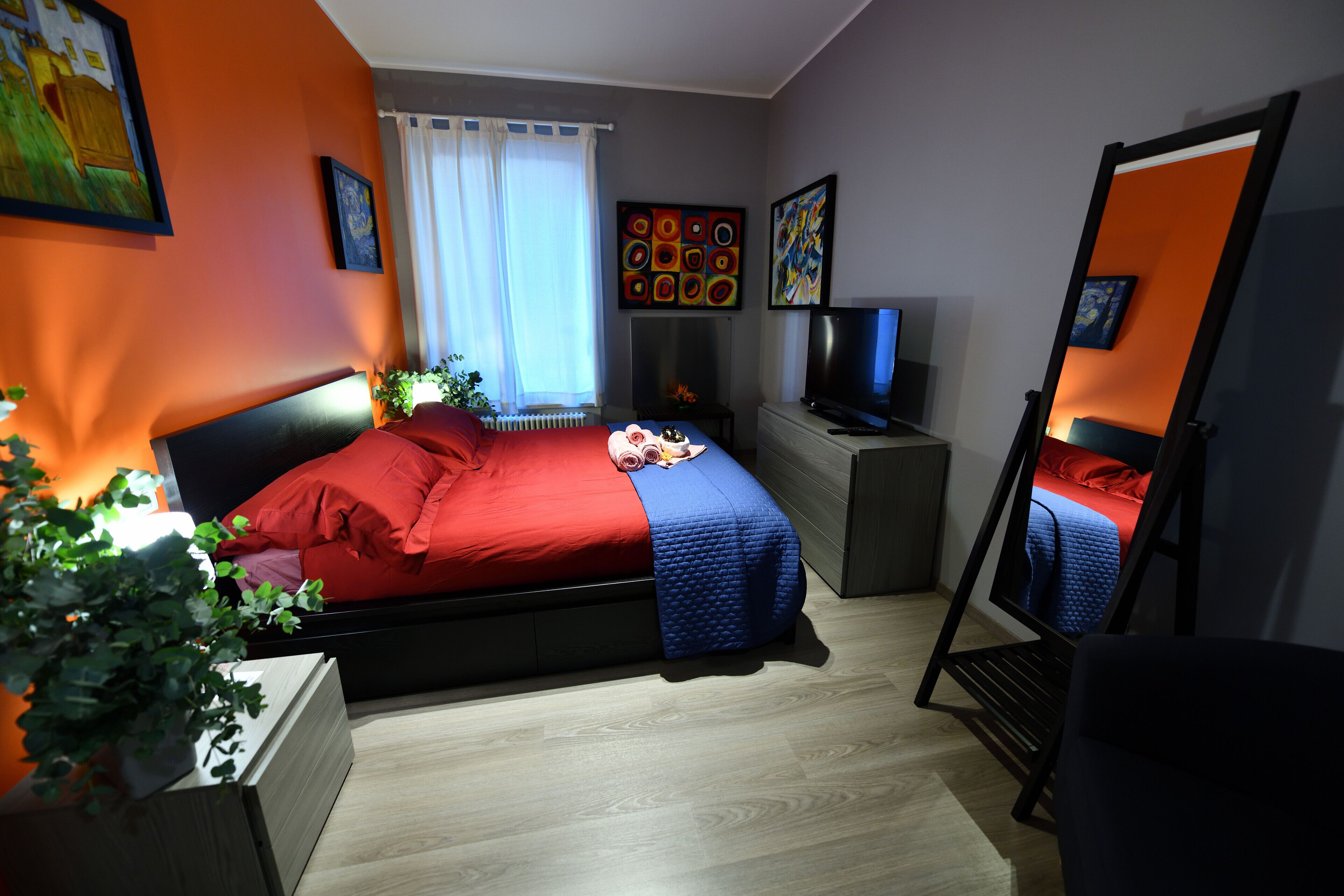 Una camera da letto con un letto, una televisione, uno specchio e opere d'arte alle pareti.