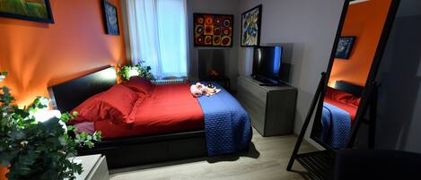 Una camera da letto con un letto, una televisione, uno specchio e opere d'arte alle pareti.