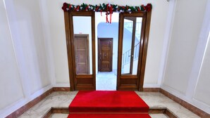 Un escalier recouvert d’un tapis rouge menant à une porte ornée de guirlandes festives.