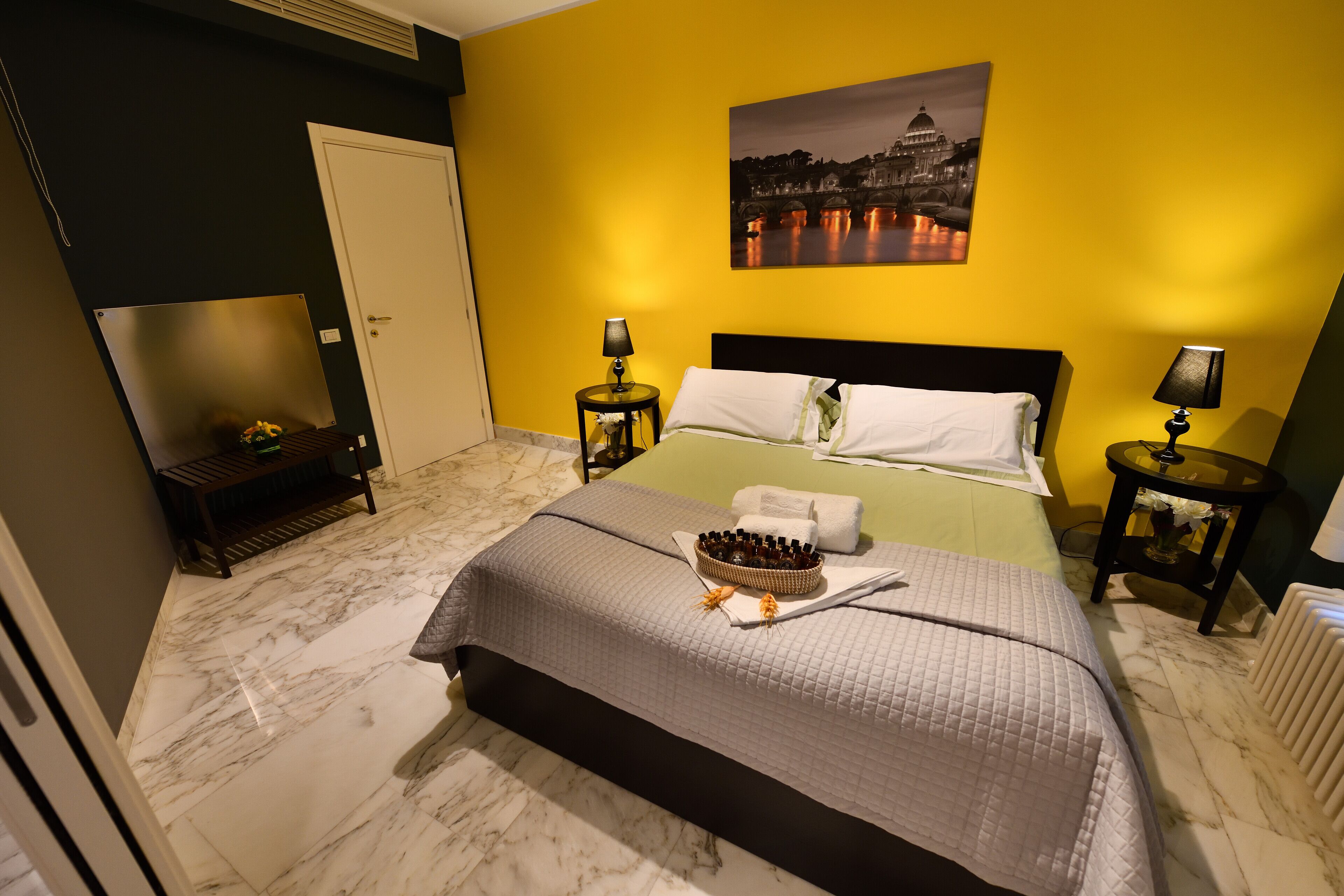 Una habitación de hotel con una cama, dos mesitas de noche, un atril, un cuadro y suelo de mármol.