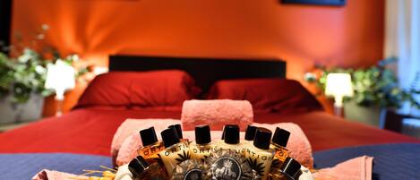 A neatly made bed with a decorative centerpiece of perfume bottles, a red headboard, and two framed artworks on the wall.