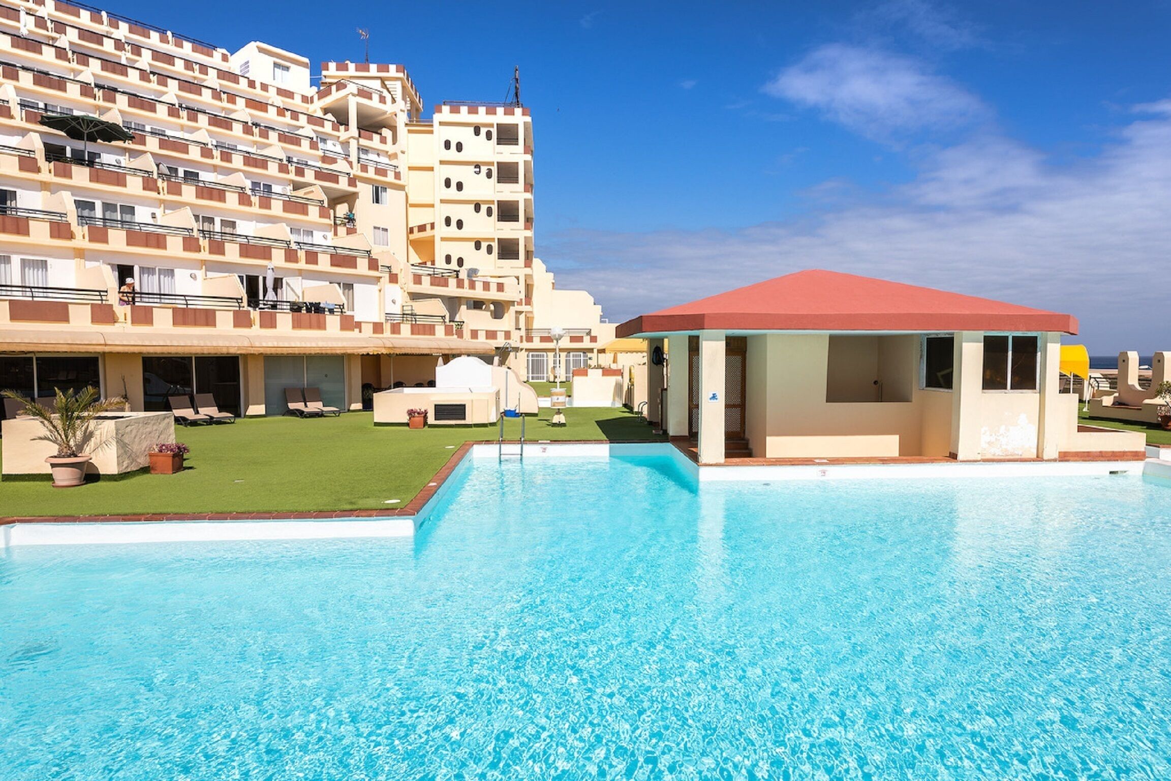 A hotel with a swimming pool, multiple balconies, and a red-roofed structure.