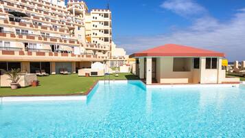 A hotel with a swimming pool, multiple balconies, and a red-roofed structure.