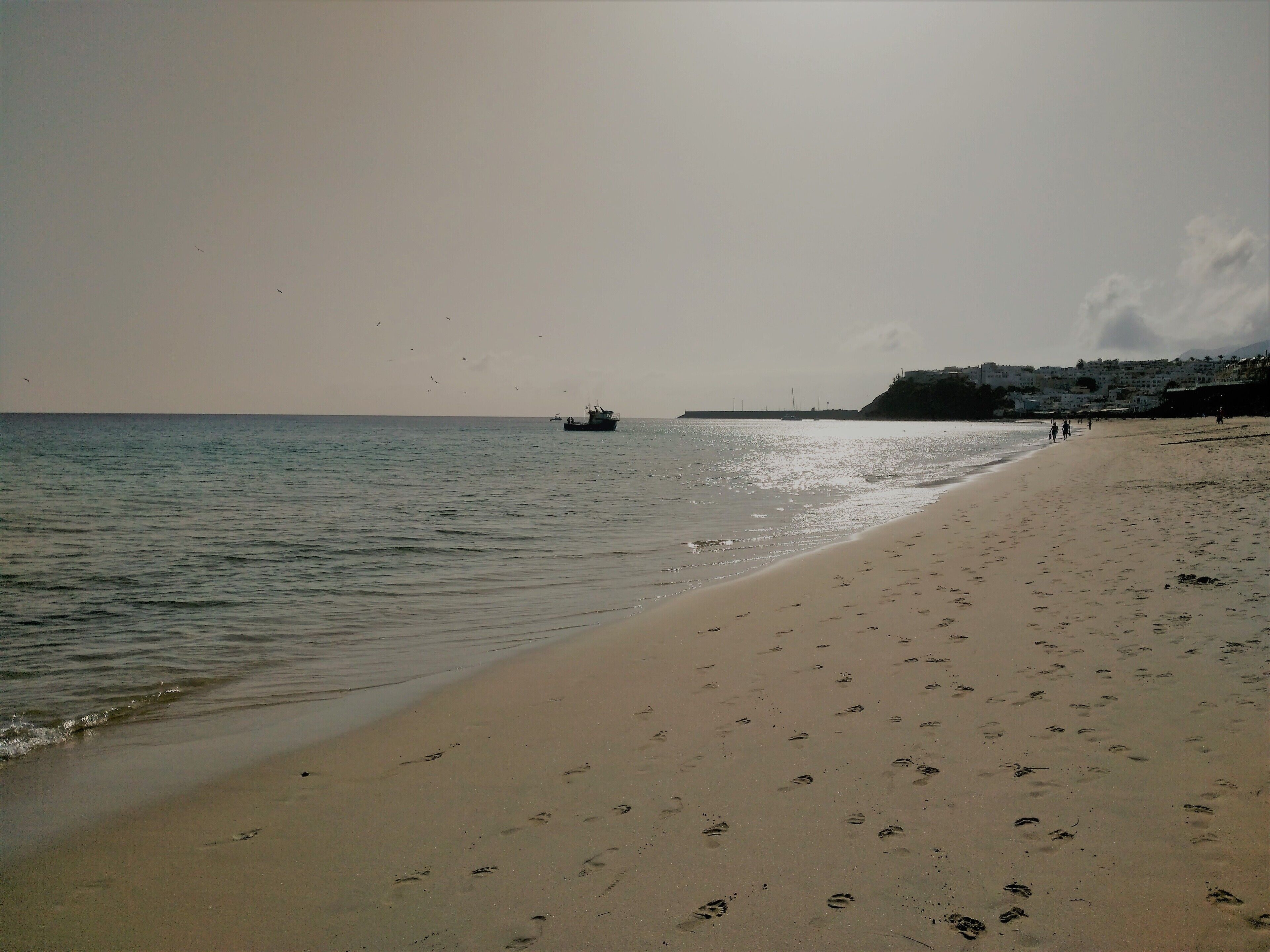 Una playa con huellas, un bote y una costa lejana con edificios.