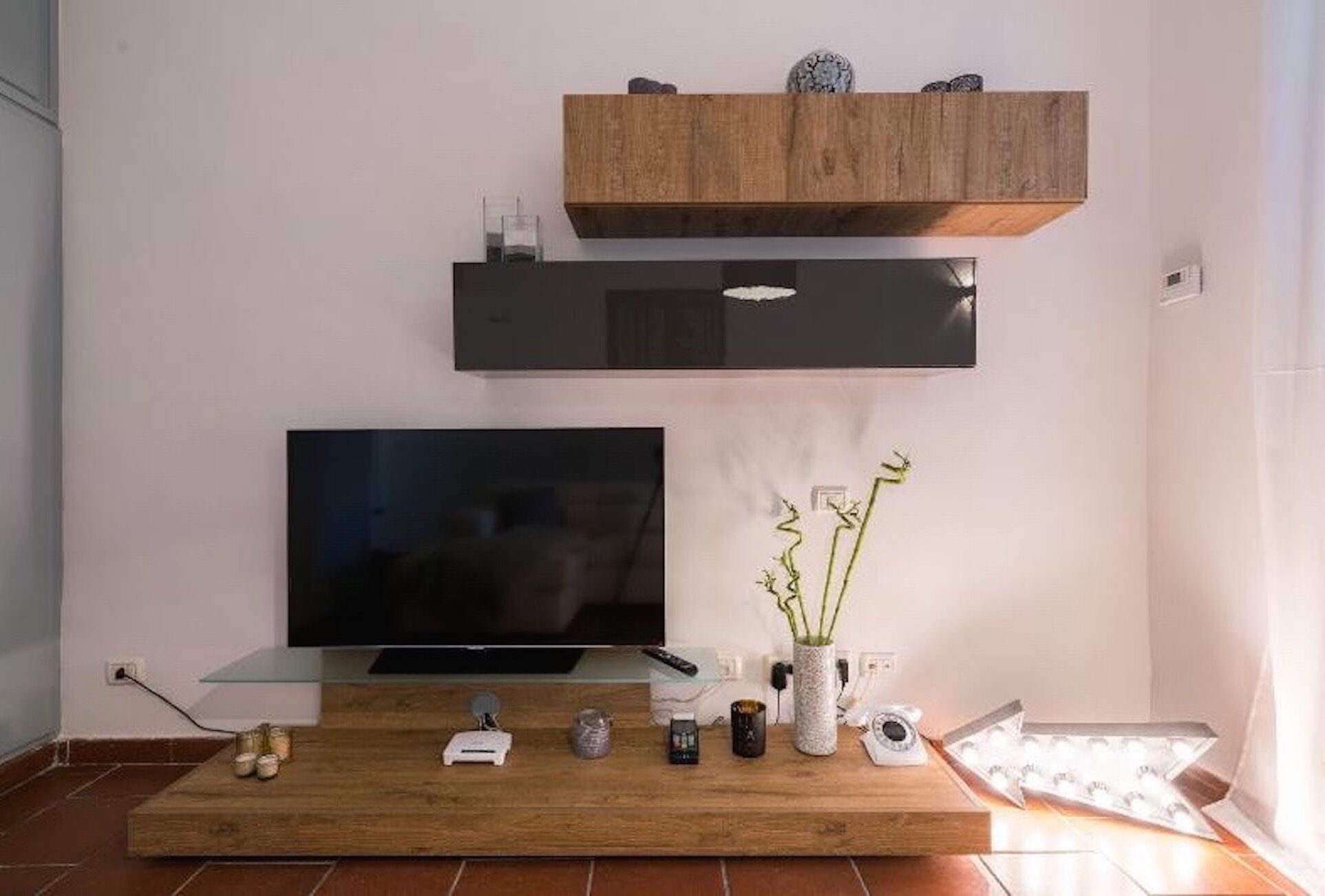 A modern living room with a flat-screen TV on a glass table, a wooden entertainment unit above, and a small plant on the table.