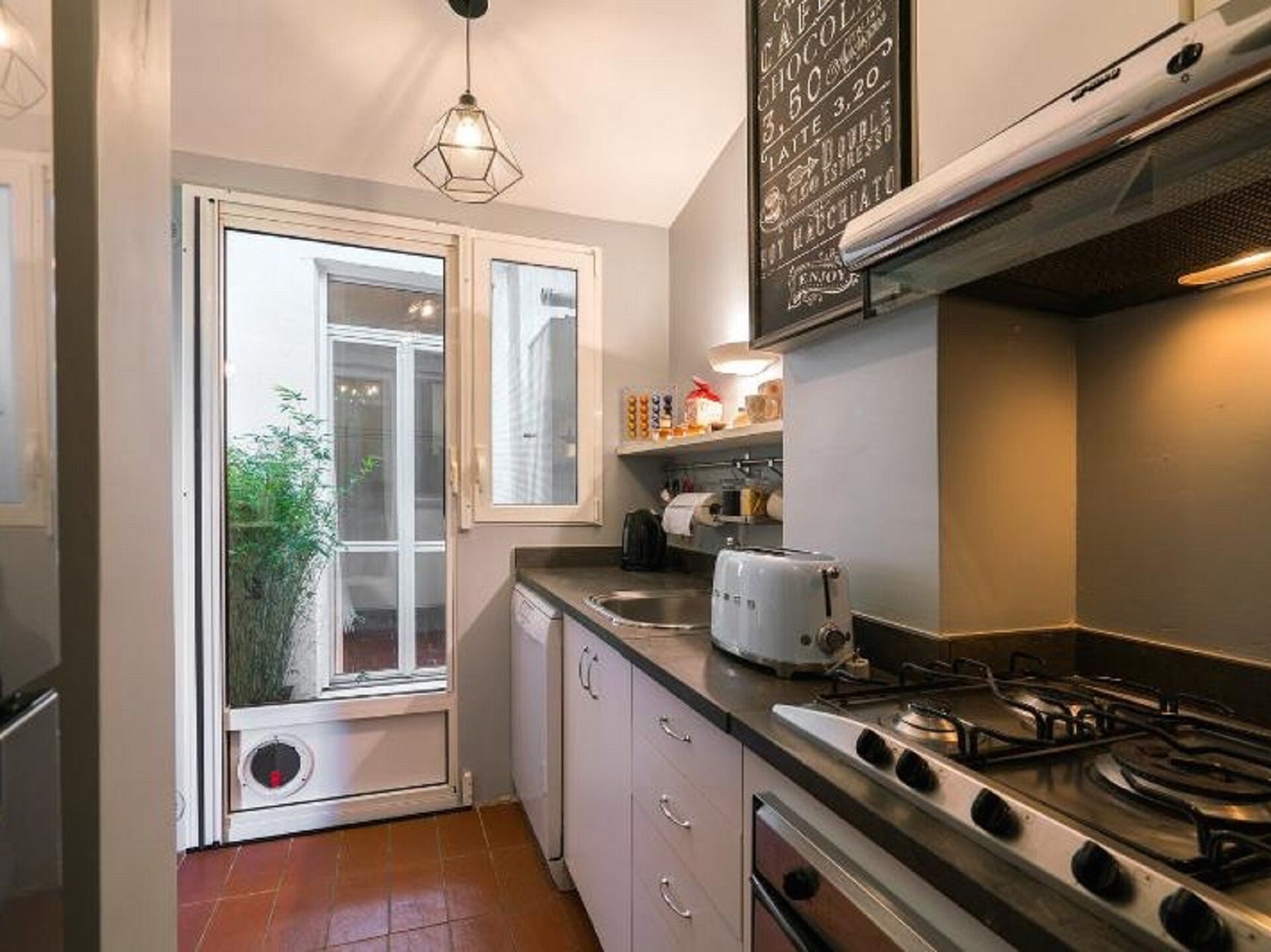 A compact kitchen with a gas stove, a toaster, and a window with a view of greenery outside.