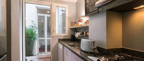 A compact kitchen with a gas stove, a toaster, and a window with a view of greenery outside.