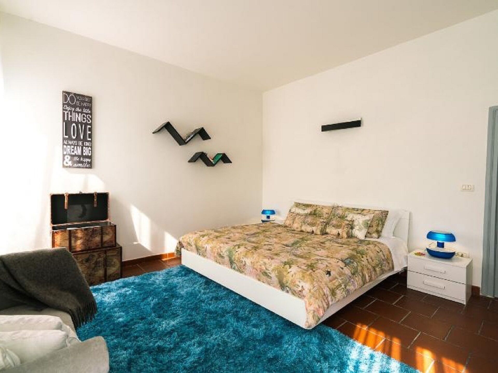 A bedroom with a bed, a blue rug, a chair, a desk, and a wall with motivational quotes.