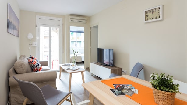 A modern living room with a sofa, a dining table, a TV, and a small side table with a plant. - Brand New Apartment Near Camp Nou & Fira Barcelona (L'Hospitalet de Llobregat)