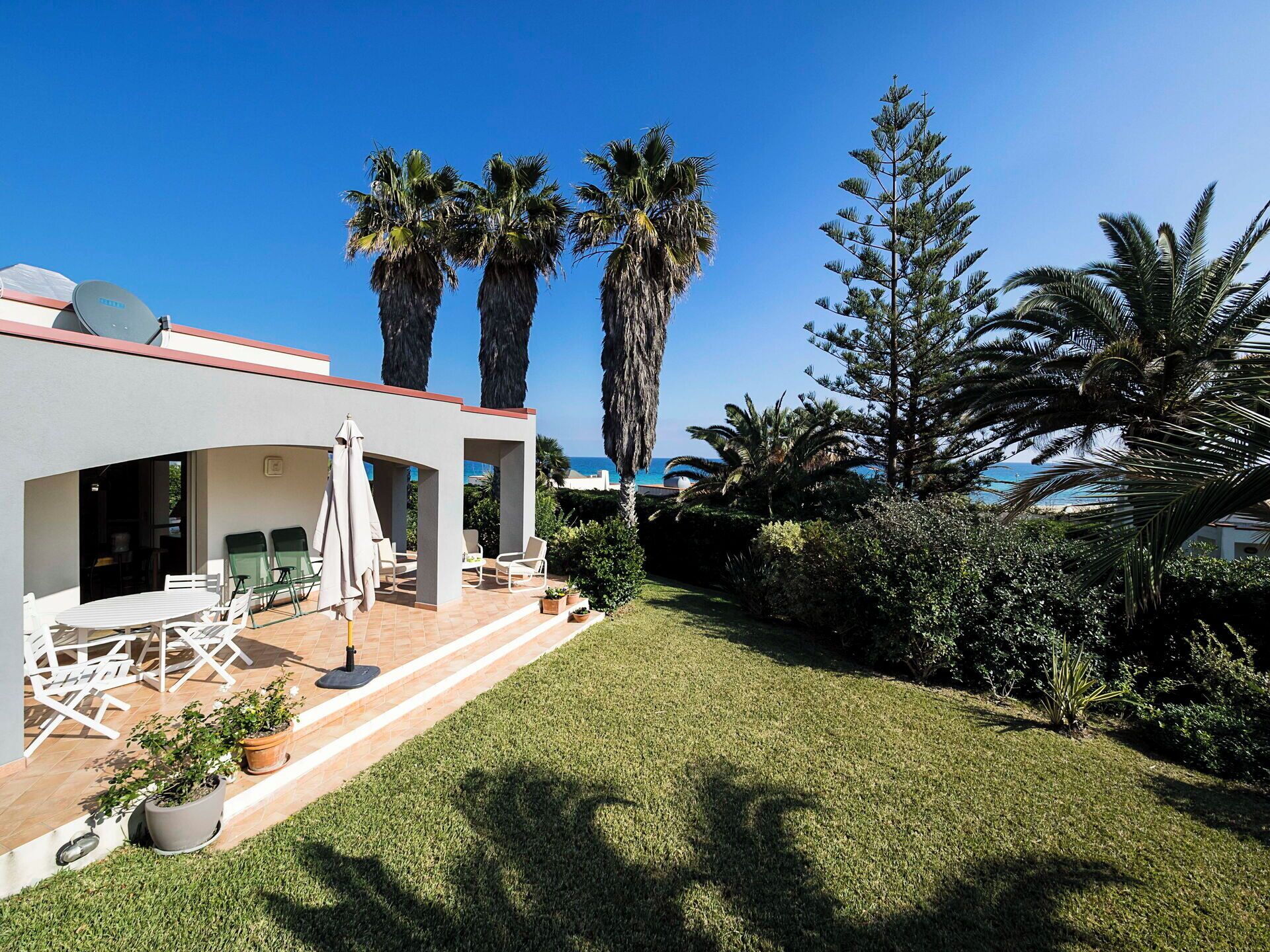Une maison moderne dotée d’un patio aménagé avec du mobilier d’extérieur et offrant une vue sur la mer.
