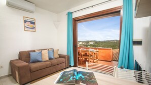 Una habitación con un sofá marrón, una mesa con una revista y vistas a un balcón con mesa y sillas.