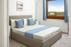 A bedroom with a bed, a nightstand, a framed picture on the wall, and a window with curtains. - Beautiful apartment sea view - Residence Eolo (Santa Teresa Gallura)